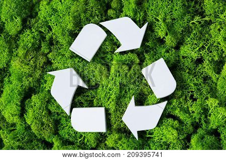 Top view of white recycle eco symbol on green moss with copy space. High angle view of recycled sign and eco concept on green background. Recycling and conservation of the environment sign.