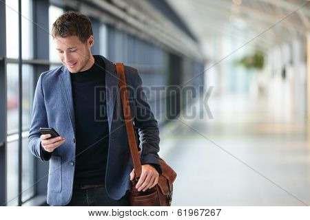 Man on smart phone - young business man in airport. Casual urban professional businessman using smartphone smiling happy inside office building or airport. Handsome man wearing suit jacket indoors.