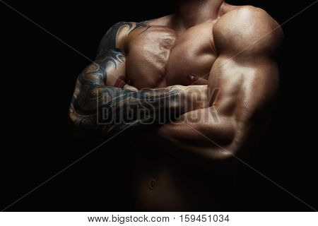 Athletic man's torso. Unrecognizable male fitness model show naked muscular body. Strong hands, chest and shoulder muscles and biceps. Studio shot on black background, low key. Bodybuilding concept