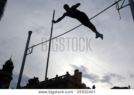 Silhouetted athlete clearing the bar during a pole vault event