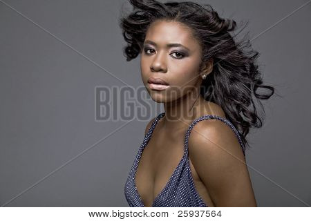 Beautiful young African-American fashion model in blue dress, with hair fluttering on wind.