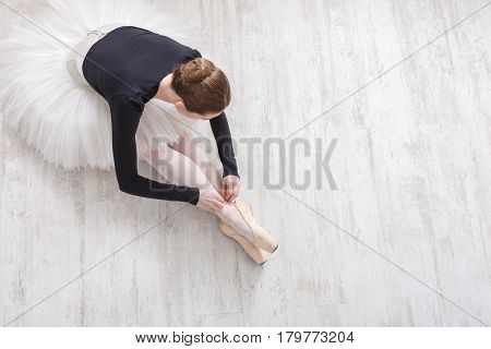 Graceful young ballerina in pointe shoes at white wooden floor background, top view from above with copy space. Ballet practice and stretching. Back of ballet dancer.