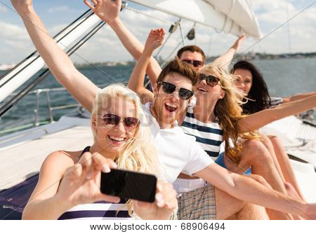 vacation, travel, sea, friendship and people concept - smiling friends sitting on yacht deck and making selfie