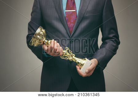 Awards ceremony. Business success. Best worker. The winner man in suit holds in front of him the award golden cup trophy in his hands.