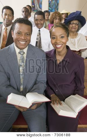 Young couple with Bibles sitting on church pews portrait