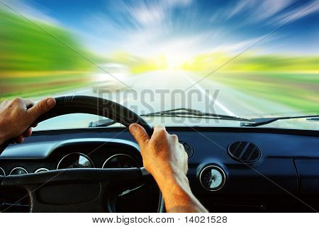 Hands on steering wheel of a car driving on an asphalt blurred road