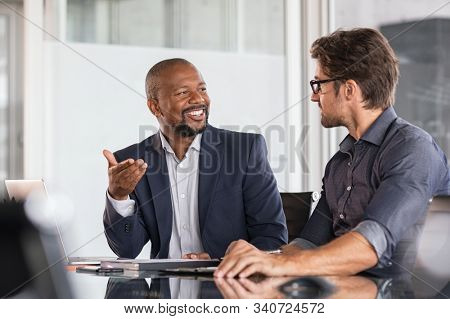 Two happy business colleagues at meeting in modern office interior. Successful african boss in a conversation with young employee in boardroom. Marketing team of two businessmen discussing strategy.