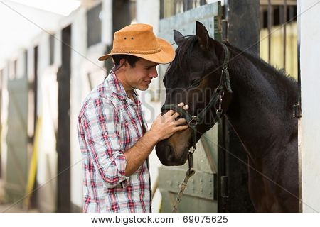 young horse breeder comforting a horse in stable