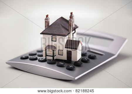 House resting on calculator concept for mortgage calculator, home finances or saving for a house