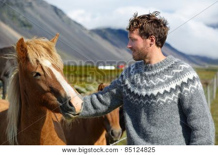 Icelandic horses - man petting horse on Iceland. Man in Icelandic sweater going horseback riding smiling happy with horse in beautiful nature on Iceland. Handsome Scandinavian model.