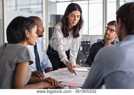 Team of multiethnic architects working on construction plans in meeting room. Engineers and designers discussing project in office. Businesswoman with business team in conference working on blueprint.