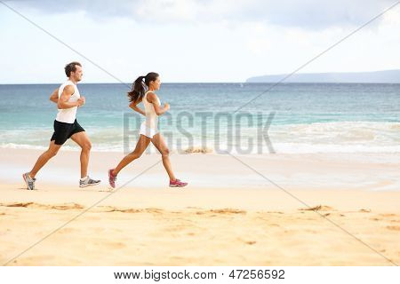 Running people - woman and man athlete runners jogging in sand on beach. Fit young fitness couple exercising healthy lifestyle outdoors. Male athlete and female fitness model training together.