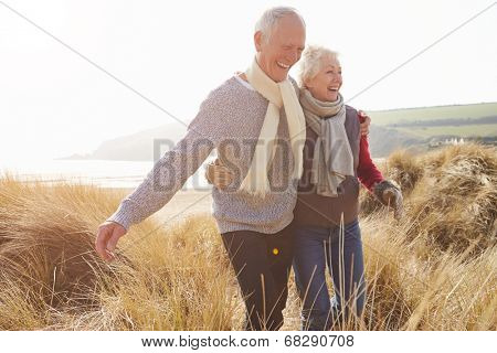 Senior Couple Walking Through Sand Dunes On Winter Beach