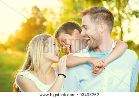 Happy joyful young family father, mother and little son having fun outdoors, playing together in summer park, countryside. Mom, Dad and kid laughing and hugging, enjoying nature outside. Sunny day