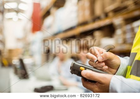 Close up of manager wearing yellow vest using handheld in a large warehouse