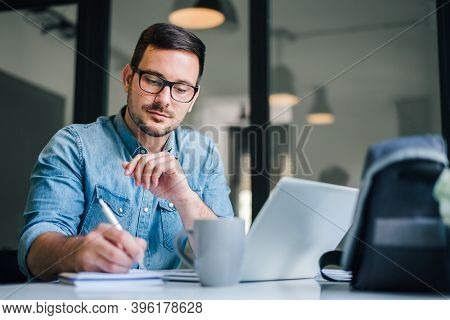 Close Up Portrait Of Handsome Man Working From Home Office Taking Reading And Writing Notes In Note 