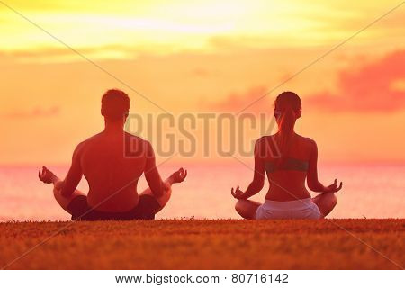 Meditation yoga couple meditating at serene beach sunset. Girl and man relaxing in lotus pose in calm zen moment in the ocean during yoga holiday class at resort retreat.