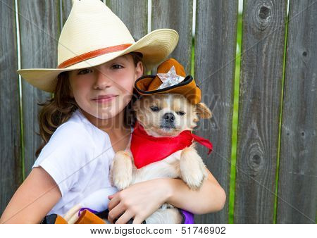 Beautiful cowboy kid girl holding chihuahua dog with sheriff hat in backyard wooden fence