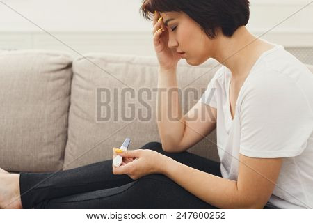 Unhappy Young Woman With Pregnancy Test Sitting On Sofa At Home. Family Issues And Maternity Concept