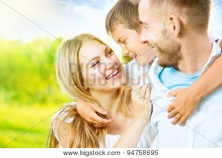 Happy joyful young family father, mother and little son having fun outdoors, playing together in summer park, countryside. Mom, Dad and kid laughing and hugging, enjoying nature outside. Piggyback