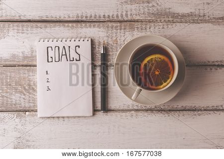 Goals concept. Notebook with goals list, cup of tea on wooden table. Motivation strategy write idea success solution concept. Top view. Retro toned image.