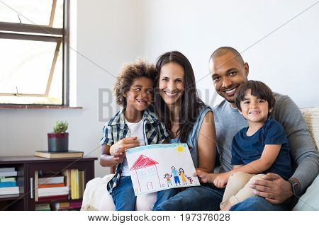 Proud parents showing family painting of son sitting on sofa at home. Smiling mother and father with children?. Black boy with his family at home showing a painting of a happy multiethnic family.