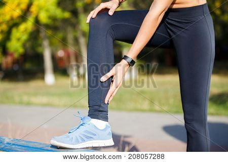 Female runner touching cramped calf at morning jogging. Achilles tendon pain or injury concept background