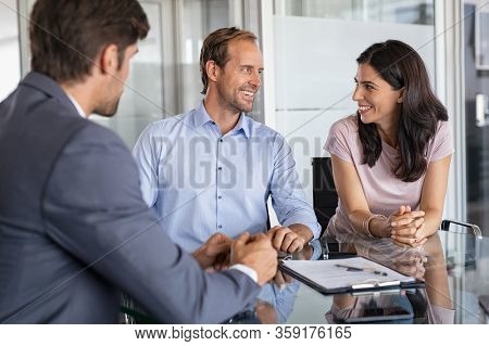 Mature smiling couple meeting financial advisor for investment at office. Financial consultant presents bank investments to man and happy woman. Middle aged couple consulting their bank agent. Saving