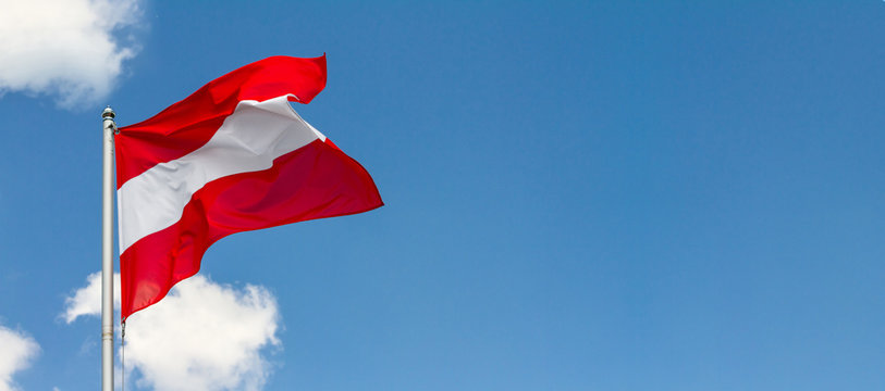 Flag of Austria waving in the wind on flagpole against the sky with clouds on sunny day, banner, close-up