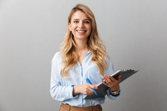 Photo of gorgeous blond secretary woman with long curly hair writing down notes in clipboard while working in office