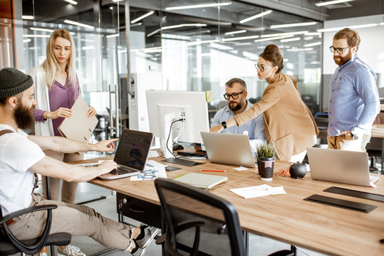 Group of diverse colleagues working on the computers in the modern office or coworking space, bearded hipster as a programmer writing code