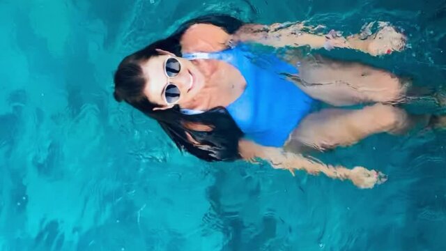 Beautiful woman swimming in the pool in blue and white stripped swimming suite and sunglasses High vertical quality 4k footage