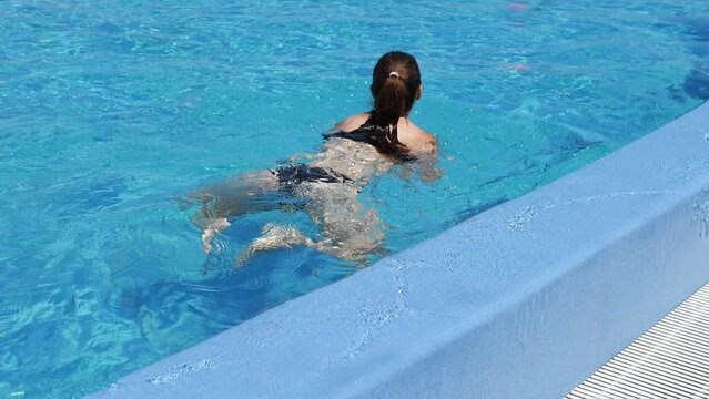 Slow motion footage of a woman sitting in a pool, enjoying the sun, and swimming in the pool.