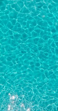 Vertical video. Blue water in the swimming pool with light reflections. Aerial footage