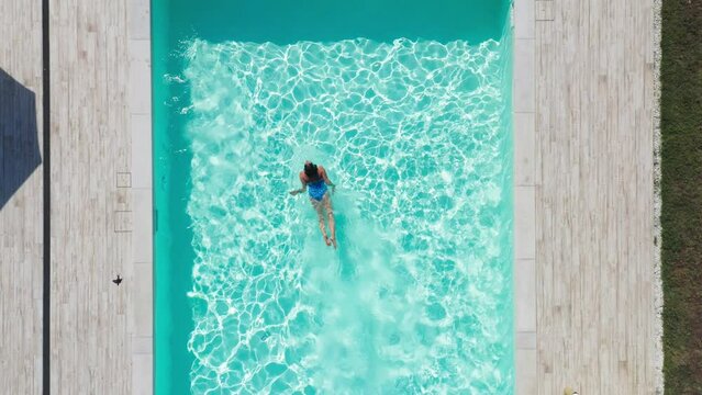 4K drone footage of woman swimming underwater in swimming pool coming to surface. 
Sports, swimming, water sports, recreation, summer vacation concept.