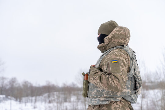 a Ukrainian military man in winter uniform, body armor and with a weapon is on combat duty. protective equipment of a soldier. infantryman with machine gun and ammunition at war in winter