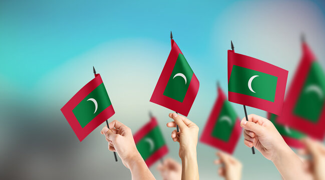 A group of people are holding small flags of Maldives in their hands.