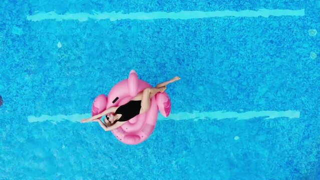 Aerial drone view of woman on pink flamingo pool float in pool in hotel. Summer holidays, enjoying summer vacations footage from above
