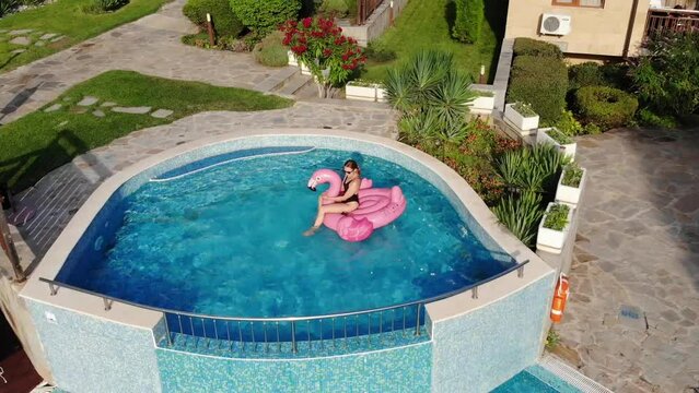 Aerial drone view of woman on pink flamingo pool float in pool in hotel. Summer holidays, enjoying summer vacations footage from above
