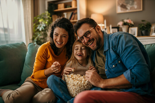 Smiling Caucasian family sitting on the couch and watching a comedy on the TV