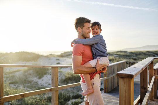 Father carrying son and walking on boardwalk at beach