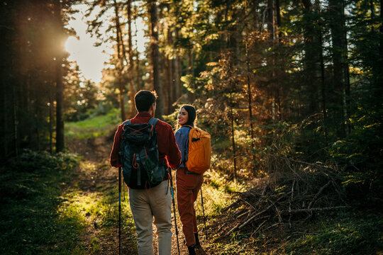 Couple with backpacks hiking together in forest during sunset