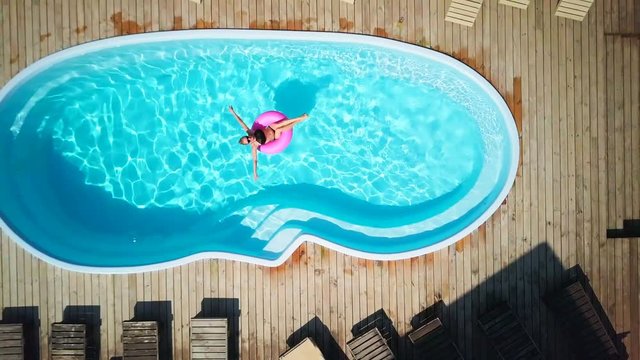 Top view fit girl enjoy pool in swimming circle sunny day sunrise drone footage