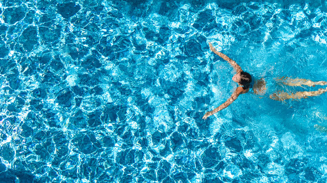 Aerial drone view of active girl in swimming pool from above, yong woman swims in blue water, tropical vacation, holiday on resort concept
