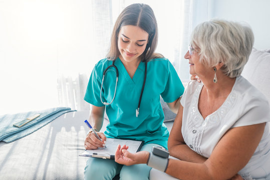 Nurse measuring blood pressure of senior woman at home. Smiling to each other.