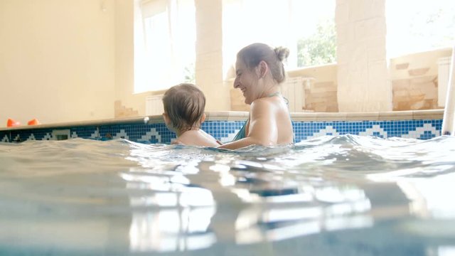 4k footage of happy young mother with toddler boy playing and enjoying swimming in pool at gym