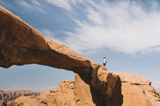 Side view of unrecognizable traveler taking photos of Wadi rum desert from top of rocky cliff against cloudy sky on sunny day in Jordan