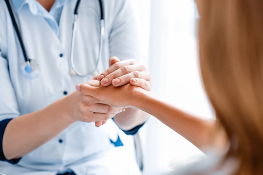 Close up of doctor holding young woman's hand at hospital