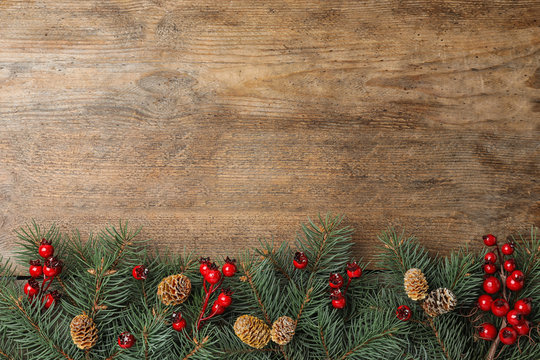 Flat lay composition with fir branches and berries on wooden background, space for text. Winter holidays