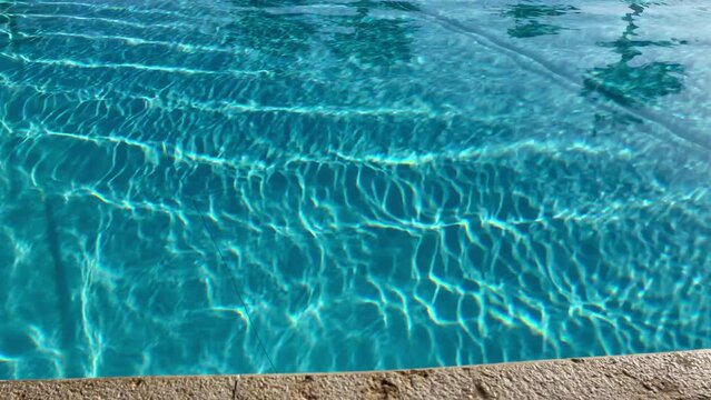 View of blue swimming pool from the bottom to the sky with the palm trees landscape. Shaking water in the swimming pool with palm trees reflections and sun glare footage